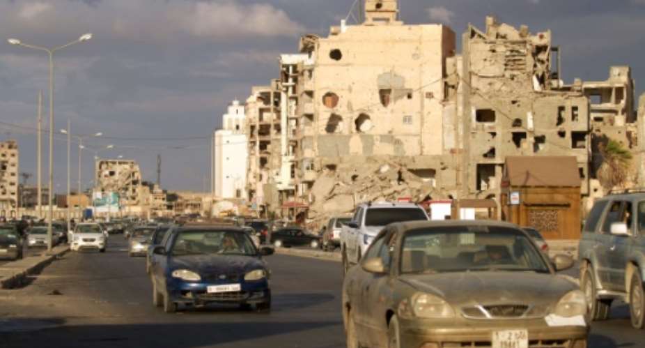 Cars drive near shell-pocked buildings in Libya's eastern coastal city of Benghazi on October 23, 2020, after a ceasefire agreement was signed between the country's warring factions.  By Abdullah DOMA AFP