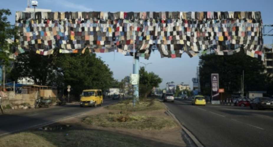 Cars drive under a billboard covered with clothes as part of the Baleboard project in Accra.  By CLAUDIA LACAVE (AFP)