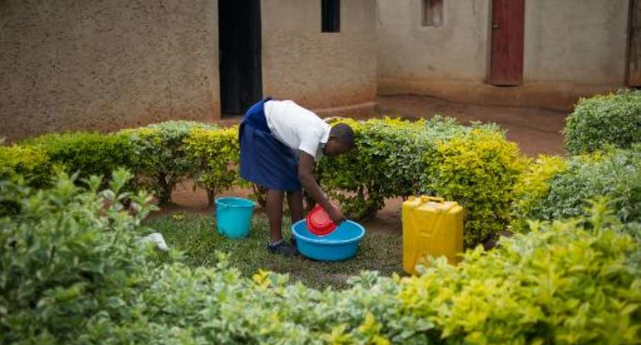 Sofia, 19 year-old daughter of a rape victim, washes utensils outside her home on the outskirts of Kigali, Rwanda on March 14, 2014.  By Phil Moore AFP