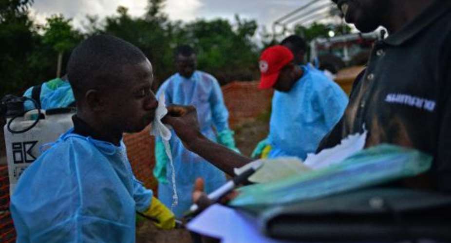 Sierra Leone government workers are disinfected after loading the bodies of Ebola victims onto a truck at a clinic in Kailahun, on August 14, 2014.  By Carl de Souza AFPFile