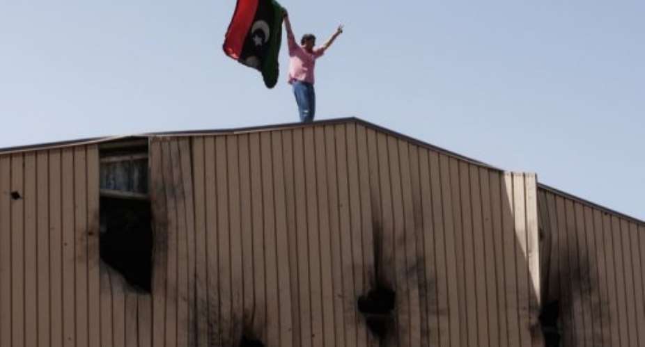 A man waves a Libyan rebel flag on top of bullet riddled warehouse in Benghazi today.  By - AFP