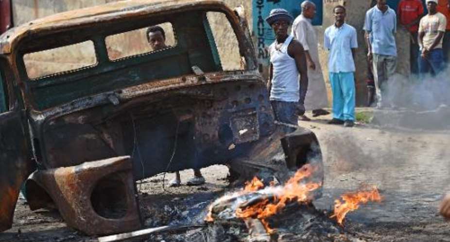 Protestors opposed to Burundian President Pierre Nkurunziza's third term stand beside a burning vehicle during a demonstration in the Buyenzi neighborhood of Bujumbura on May 26, 2015.  By Carl De Souza AFP