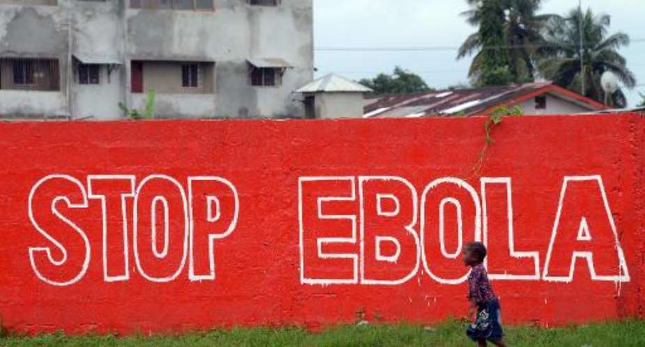 A girl walks past a slogan painted on a wall in Monrovia on August 31, 2014.  By Dominique Faget AFPFile