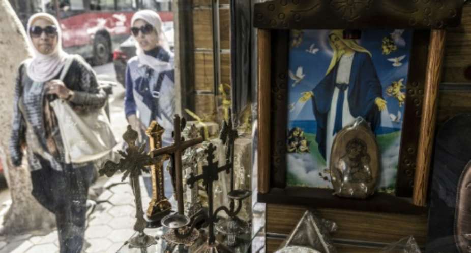 Egypian women walk past a church's paraphernalia shop displaying crucifixes and images of Christ and Coptic Orthodox religious figures in Cairo's northern suburb of Shubra, in April 2017.  By KHALED DESOUKI AFPFile