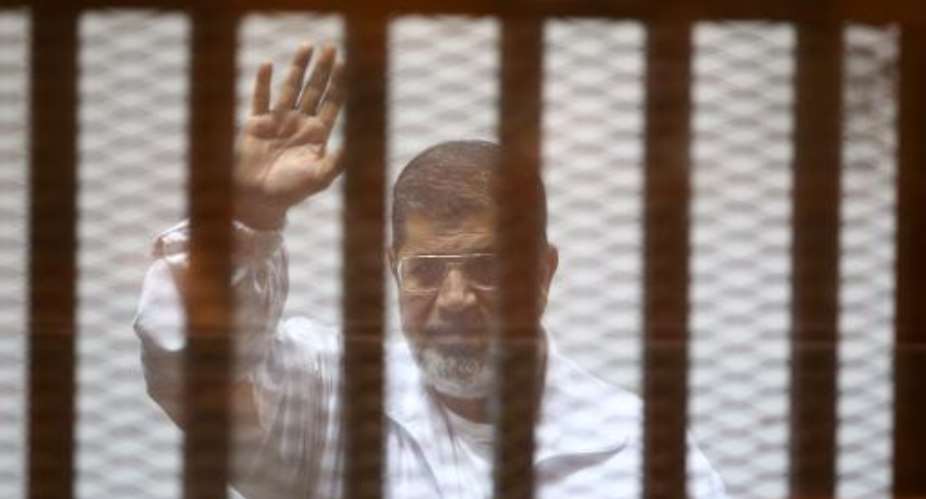 Egypts deposed Islamist president Mohamed Morsi waves inside the defendant’s cage during a trial at the police academy in Cairo on December 7, 2014.  By Ahmed Ramadan (AFP/File)