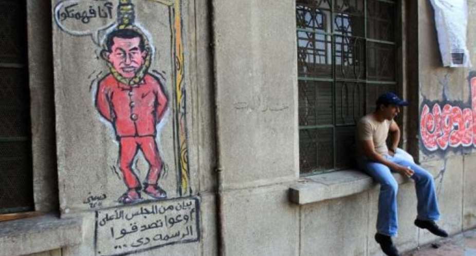 An Egyptian man sits close to graffiti depicting former president Hosni Mubarak hanging at the gallows.  By Khaled Desouki AFP