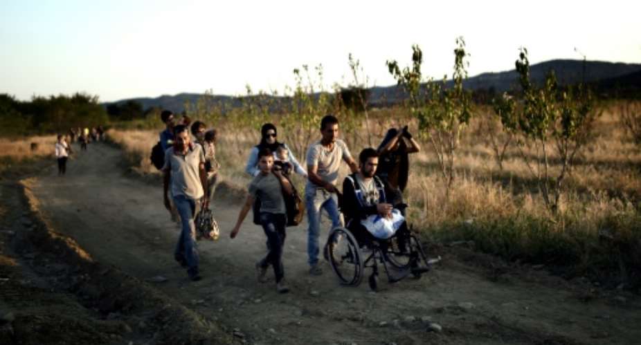 A Syrian man who lost his legs after shelling near Damascus is helped by other migrants after crossing the border from Greece to Macedonia on August 29, 2015.  By Aris Messinis AFP