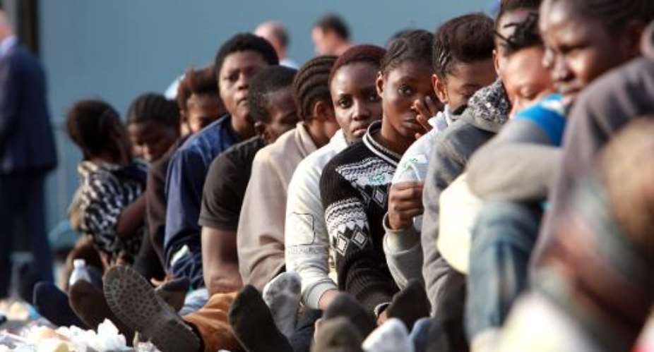 Migrants sit in line after disembarking from the Royal Navy's HMS Bulwark after arriving on the Italian island of Sicily, on June 8, 2015.  By Giovanni Isolino AFP