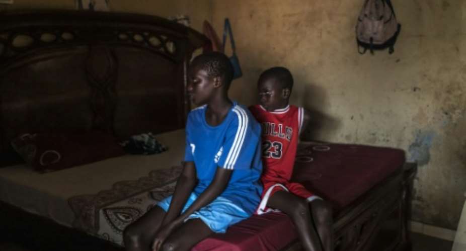 Fallou (L) and Bara (R), who lost their mother in 2024 when her pirogue capsized, watch TV at their home in Mbour, Senegal in March 2026.  By PATRICK MEINHARDT (AFP)