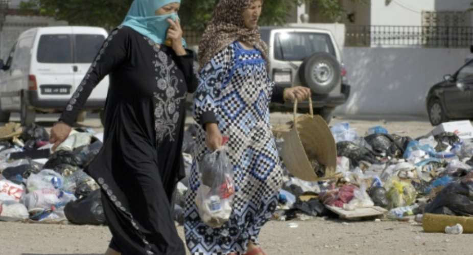 Women walk past rubbish left on the road in the town of Den Den, west of the capital Tunis.  By Salah Lahbibi AFP