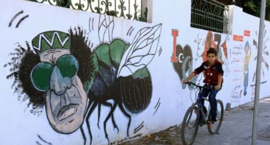 A Libyan boy cycles past graffiti depicting former strongman Moamer Kadhafi painted on a wall in Tripoli,.  By Mahmud Turkia AFPFile