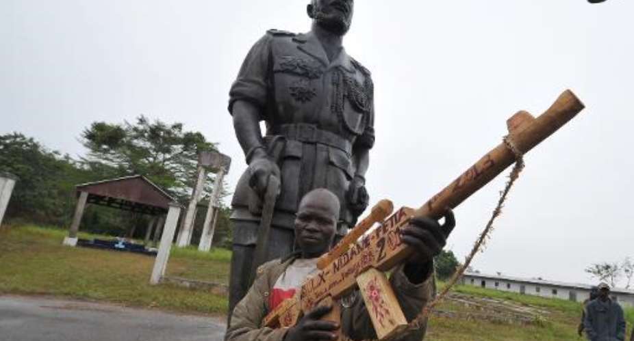 A former member of the Seleka rebel group poses with his wooden weapon next to a statue of the former Central African Republic Jean-Bedel Bokassa in Beringo, on March 3, 2014.  By Sia Kambou AFP