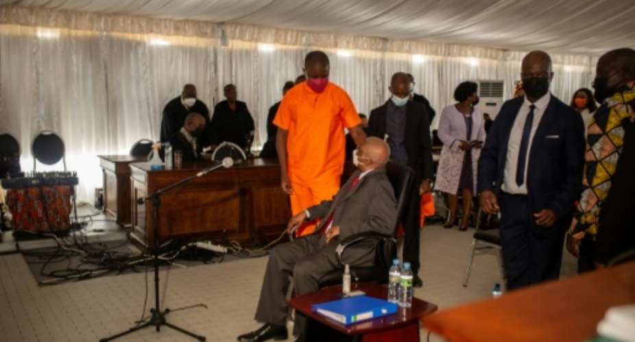 Former president Armando Guebuza, seated, talks to his son Ndambi Guebuza, wearing an orange prison uniform. The younger Guebuza is a major defendant in the long-awaited trial, which is unfolding in a marquee in a high-security jail.  By Alfredo Zuniga AFP