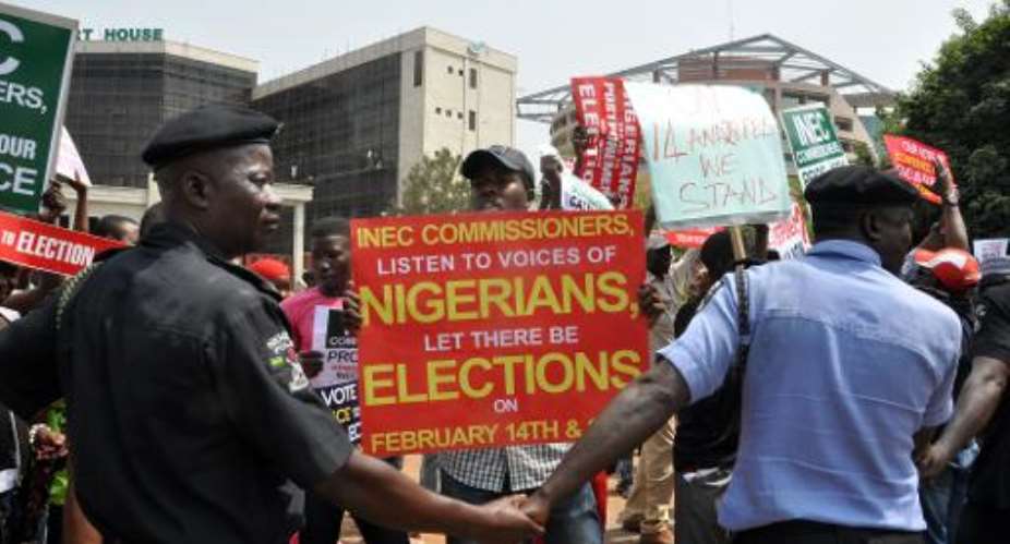 Police officers holds hands to block people holding sign protesting as chairman of the Independent National Electoral Commission  announced that Nigeria has postponed its presidential election.  By  AFPFile