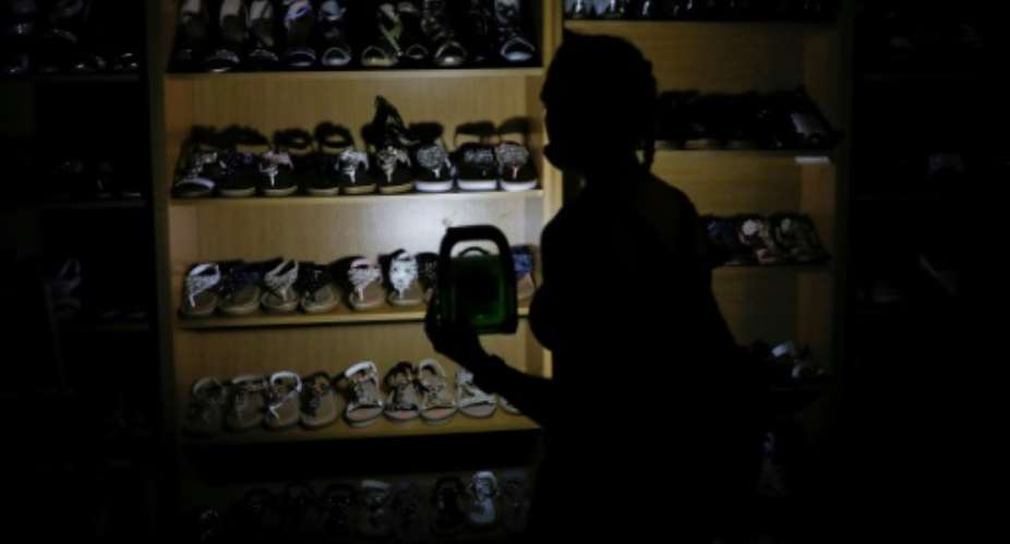 Go with the glow: A shopper uses a rechargeable LED lamp to illuminate a shoe rack.  By Phill Magakoe AFPFile