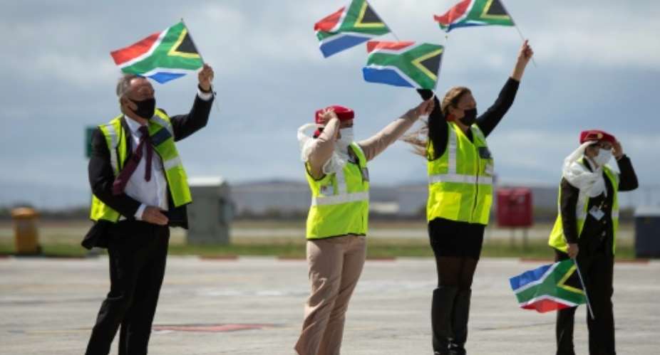 Ground crew wave flags as an Emirates airliner lands in Cape Town from Dubai, marking the end of South Africa's long ban on international flights.  By RODGER BOSCH AFP