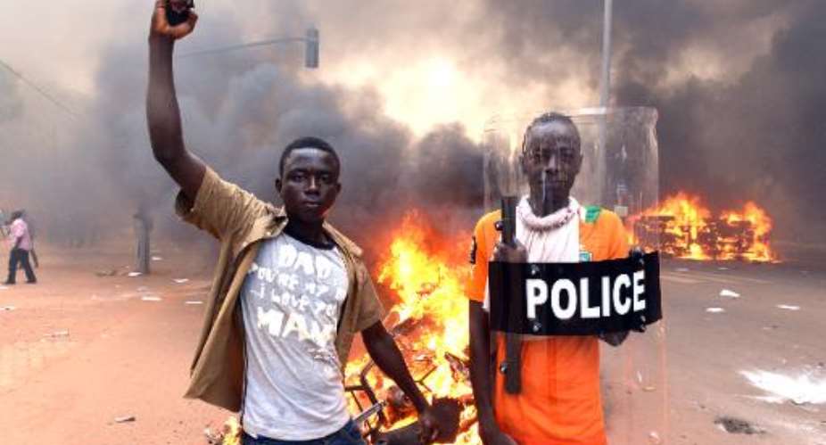 Protesters pose with a police shield outside the parliament in Ouagadougou on October 30, 2014 as cars and documents burn nearby, in a popular revolt that ousted president Blaise Compaore.  By Issouf Sanogo AFPFile