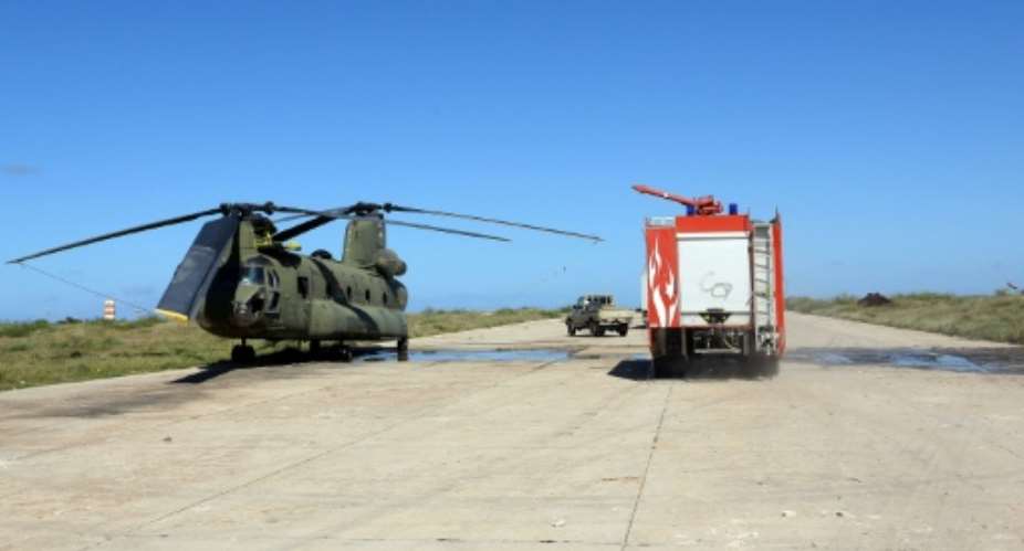 In this file photo, a firefighting truck is parked next to an Italian-built Libyan Chinook CH-47 military helicopter that was hit by shrapnel following an air strike at Mitiga International Airport in early April.  By Mahmud TURKIA AFPFile