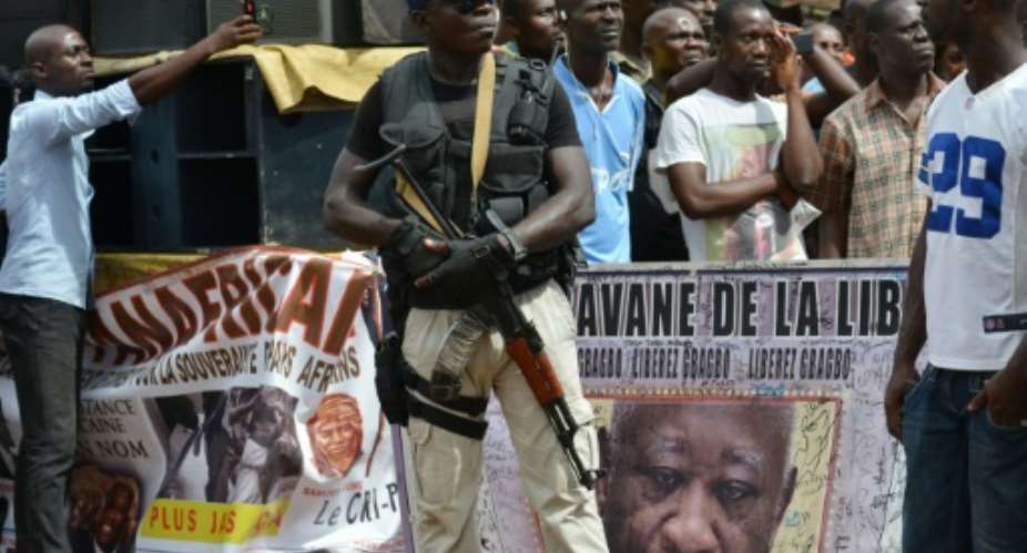 An armed man stands next to a banner featuring former Ivory Coast President Laurent Gbagbo during a meeting of the National Coalition for Change CNC party, on October 7, 2015 in Yopougon.  By Issouf Sanogo AFP