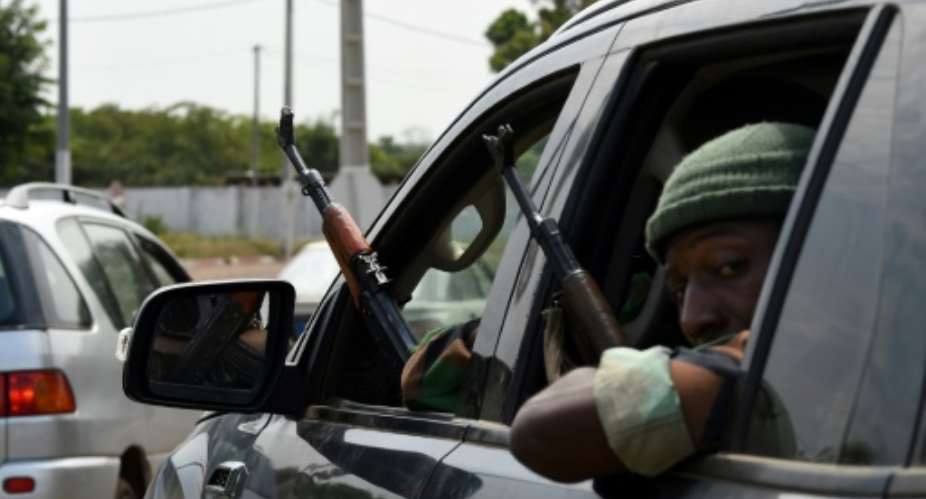 Ivory Coast soldiers sit in a car as they look outside the window with their rifles at the airport in Bouake on January 13, 2017.  By SIA KAMBOU AFP