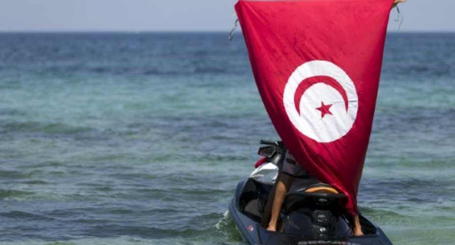 A man on a jet ski holds up a Tunisian flag at the site of a shooting attack on the beach in front of the Riu Imperial Marhaba Hotel in Port el Kantaoui, on the outskirts of Sousse, on June 28, 2015.  By Kenzo Tribouillard AFPFile
