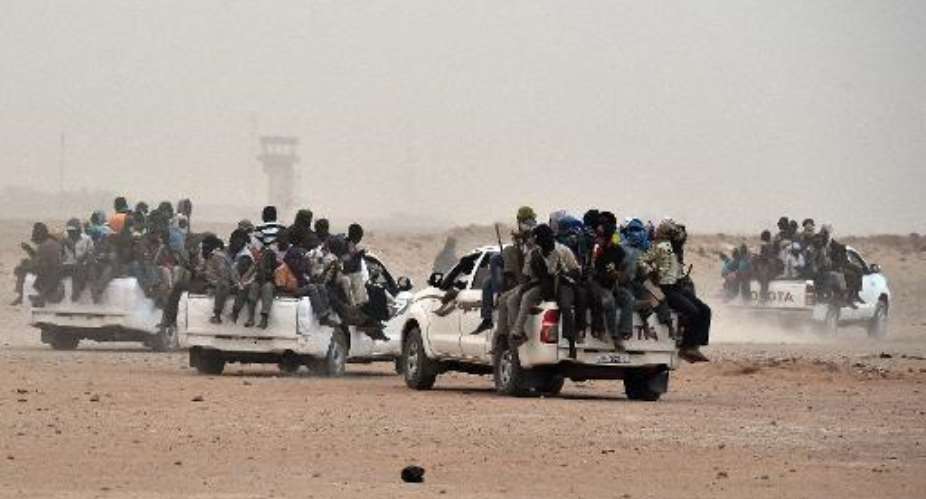 Migrants sit on pick-up trucks, holding wooden sticks tied to the vehicle to avoid falling from it, as they leave the outskirts of Agadez for Libya, from where they will try to reach Europe, on June 1, 2015.  By Issouf Sanogo AFP