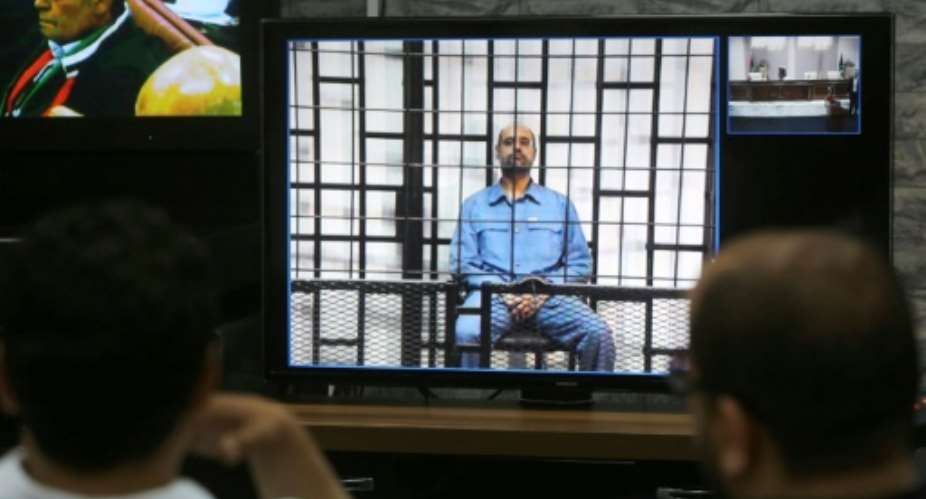 Journalists watch from a press room in Tripoli Seif al-Islam C, the son of slain Libyan dictator Moamer Kadhafi, answering his judges' questions by video conference from a prison the western Libyan city of Zintan, on May 11, 2014.  By MAHMUD TURKIA AFPFile