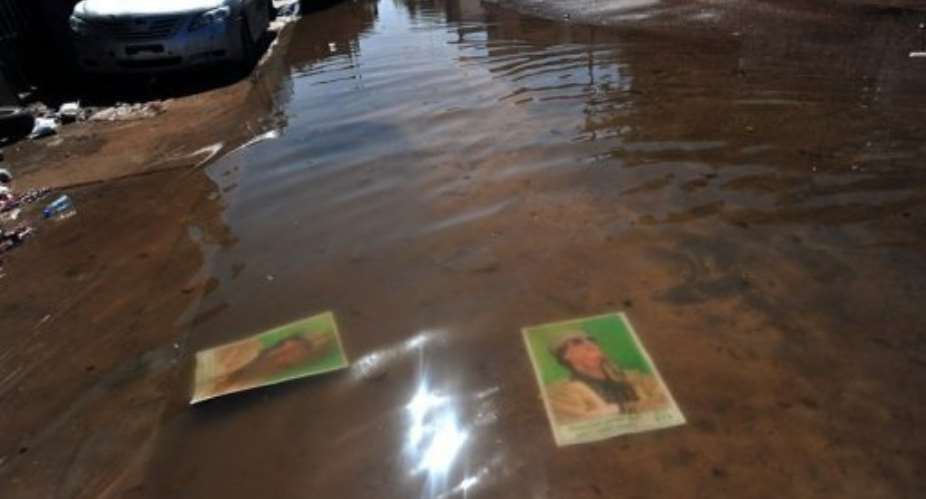 Portraits of former strongman Moamer Kadhafi are submerged in rain water at a street in Sirte on October 12.  By Aris Messinis (AFP/File)