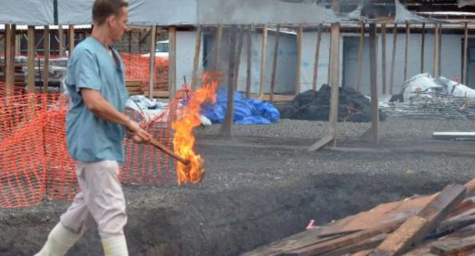 A Medecins Sans Frontieres worker burns pieces of wood on January 27, 2015 as a Ebola treatment centre in Monrovia is decommissioned.  By Zoom Dosso AFPFile
