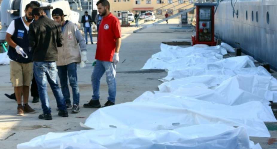 Libyan paramedics and aid workers stand next to the bodies of African migrants at a naval base in Tripoli on November 25, 2017, after more than 30 migrants died off the coast of Garabulli, 60 kilometres 40 miles east of the capital.  By MAHMUD TURKIA AFP