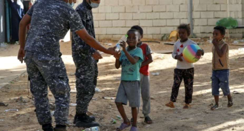 Libyan security forces hand water to children as African migrants gather at a makeshift shelter near Tripoli on October 11, 2021.  By Mahmud Turkia AFPFile