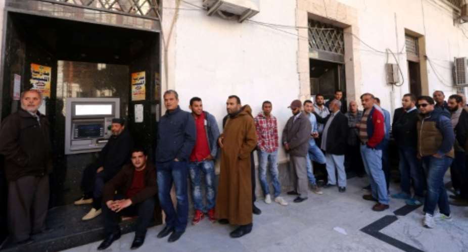 Libyans wait to withdraw money from an ATM machine outside a bank in the capital Tripoli on March 27, 2016.  By MAHMUD TURKIA AFP
