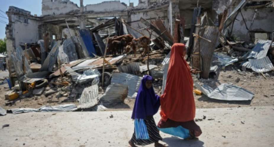 Local residents walk past the scene of a deadly December 22, 2018 car bomb attack in the Somali capital Mogadishu claimed by the jihadist group Shabaab.  By Mohamed ABDIWAHAB AFPFile