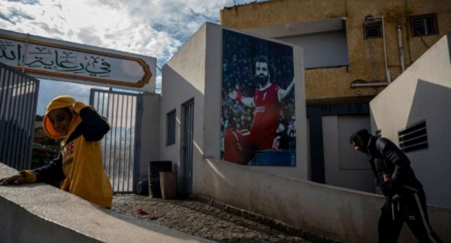 Locals pass a mural of Mohamed Salah at the entrance to the sports complex in his Egyptian home village of Nagrig.  By Khaled DESOUKI (AFP)