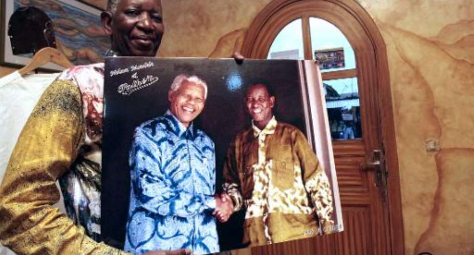 Pathe Ouedraogo poses while holding a photo of Nelson Mandela shaking hands with him on December 11, 2013 in his workshop in the Treichville district of Abidjan.  By Herve Sevi AFP