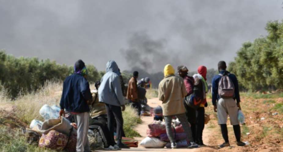 Migrants look on as smoke rises from what used to be their makeshift camp at El Amra.  By FETHI BELAID (AFP)