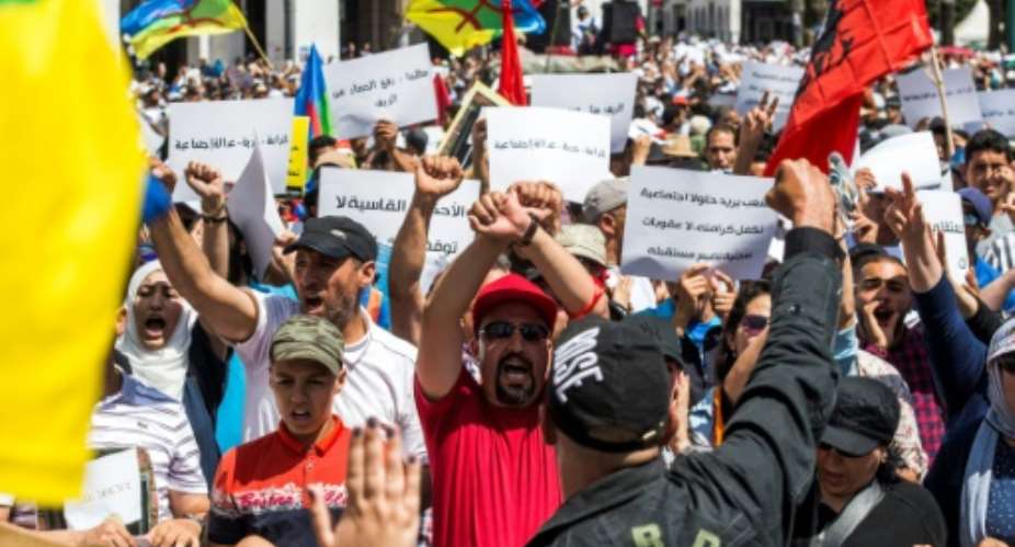 Moroccan demonstrators hold their hands up in a bound gesture while shouting slogans as they wave the Berber, or Amazigh, flag during a protest march against the jailing of Al-Hirak al-Shaabi or Popular Movement activists in Rabat on July 15, 2018.  By FADEL SENNA AFPFile