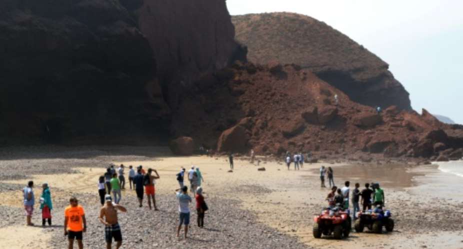 Moroccans looking at the pile of red rubble after one of the famous arches of Legzira beach collapsed at a popular beach near Morocco's South West city of Sidi Ifini.  By STRINGER AFP