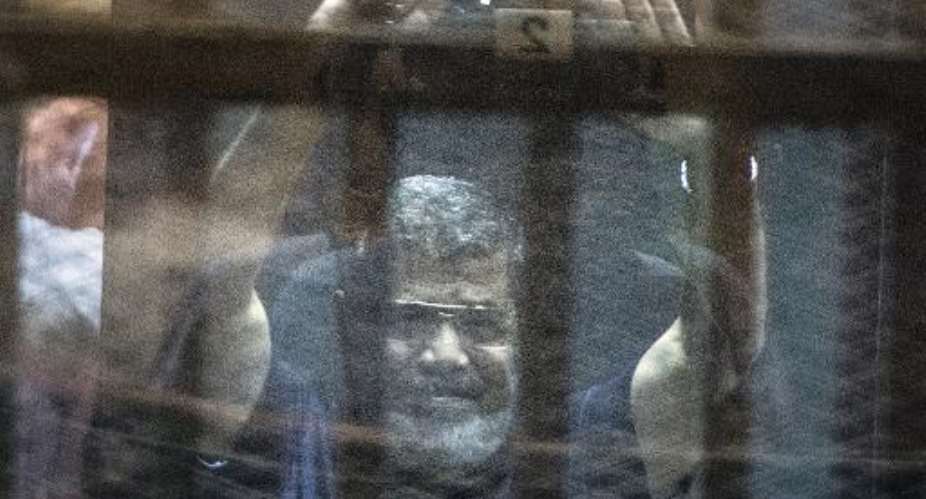 Egypt's deposed Islamist president Mohamed Morsi raises his hands from behind the defendant's cage as the judge reads out his verdict sentencing him to death at the police academy in Cairo on May 16, 2015.  By Khaled Desouki AFP