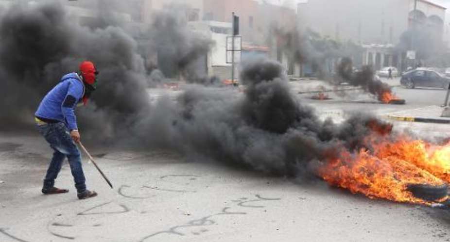 A Libyan protester stands next burning tyres as residents block a street in the capital Tripoli on March 2, 2014.  By Mahmud Turkia AFP