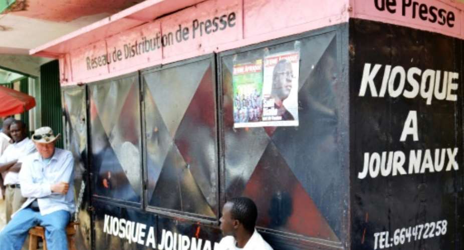 Men sit in front of a closed newspaper stand in Conakry on February 9, 2016, on a press-free day in honour of a journalist who was shot dead last week.  By Cellou Binani AFP