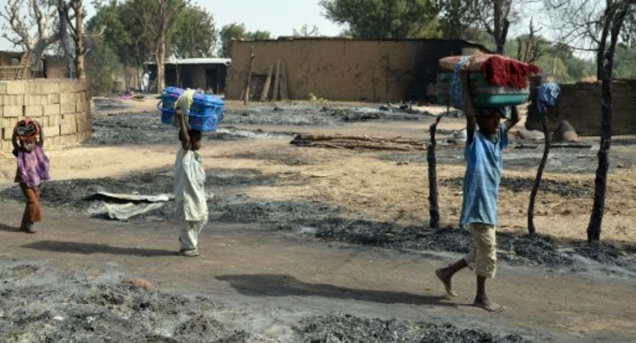 Children fleeing from Boko Haram Islamists walk past burnt houses in Mairi village on the outskirts of Maiduguri, capital of northeast Borno State, on February 6, 2016.  By  AFP