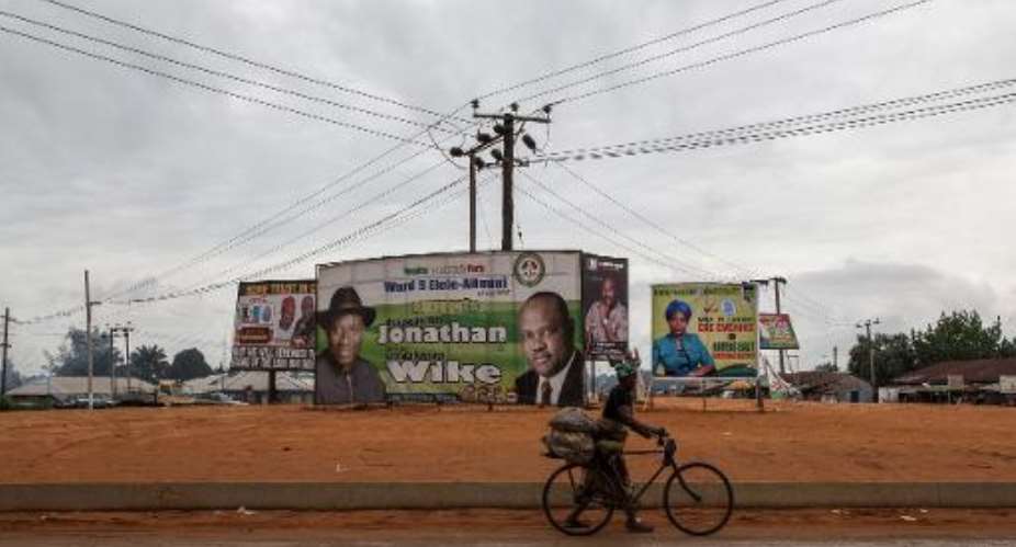 A woman walks with her bicycle past electoral campaign posters in the Rivers State town of Elele on March 27, 2015 on the eve of Nigeria's presidential election.  By Florian Plaucheur AFP