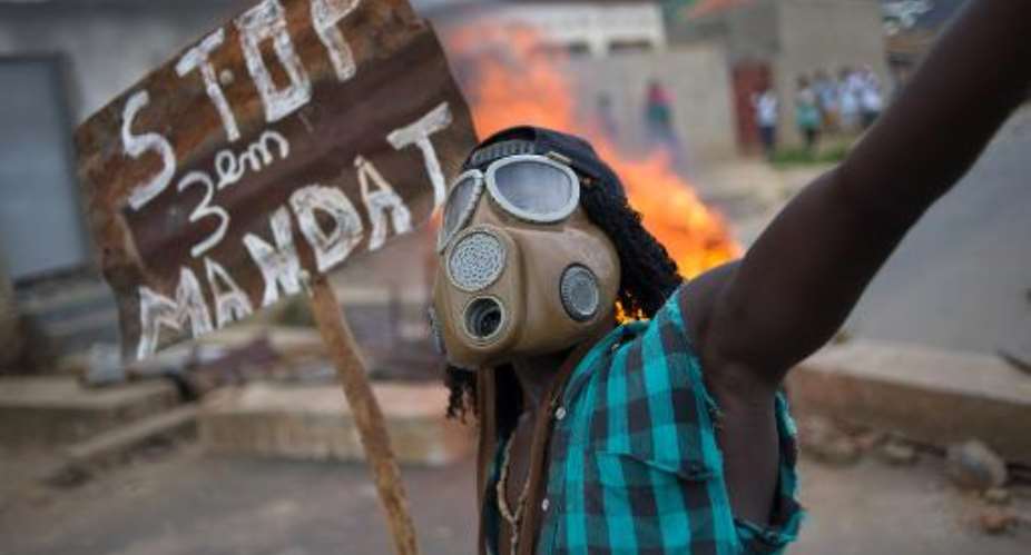 A Burundian protester wearing a gas mask and holding a sign that reads Stop the third mandate chants near a burning barricade in the Mugasa neighbourhood of Bujumbura on May 6, 2015.  By Phil Moore AFPFile