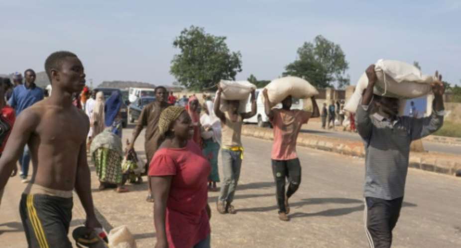 People carry bags of food during a mass looting of a warehouse in Jos, Nigeria on October 24, 2020.  By Ifiok Ettang AFP