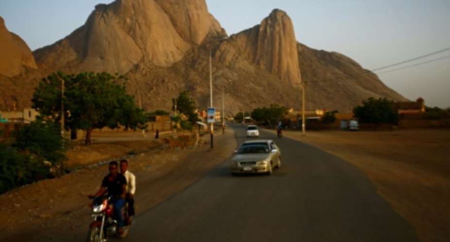 People drive on a road in Sudan's eastern border town of Kassala in front of the Taka Mountains on May 3, 2017.  By ASHRAF SHAZLY AFPFile