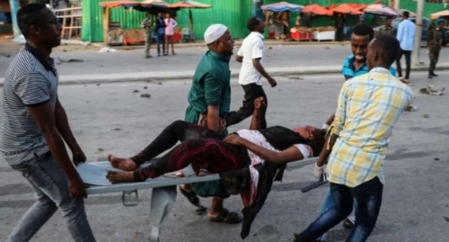People rescue a wounded person after the triple bomb attack.  By ABDIRAZAK HUSSEIN FARAH AFP