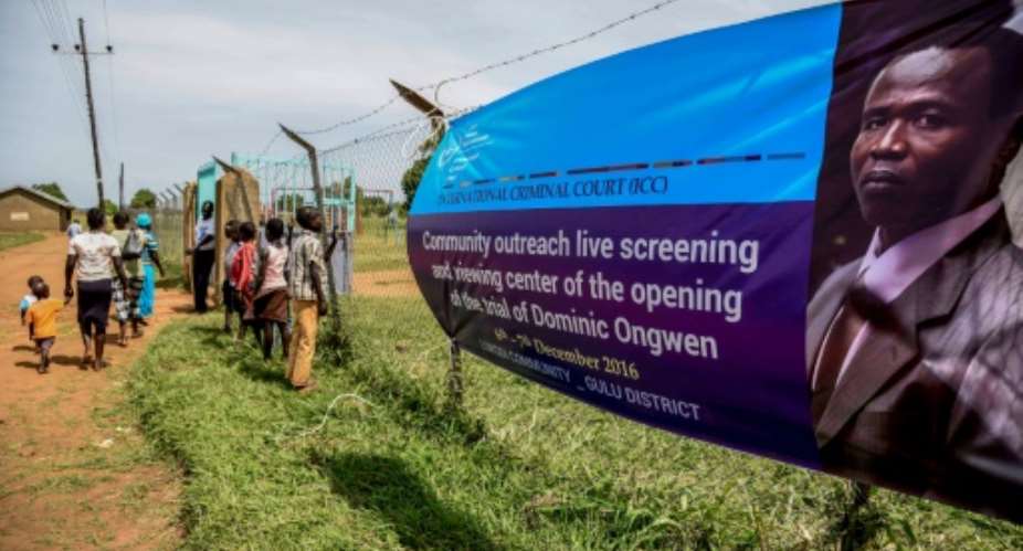 People walk near a banner of former child soldier-turned-warlord Dominic Ongwen before the screening of the start of his ICC International Criminal Court trial in Lukodi, Uganda on December 6, 2016.  By ISAAC KASAMANI AFPFile
