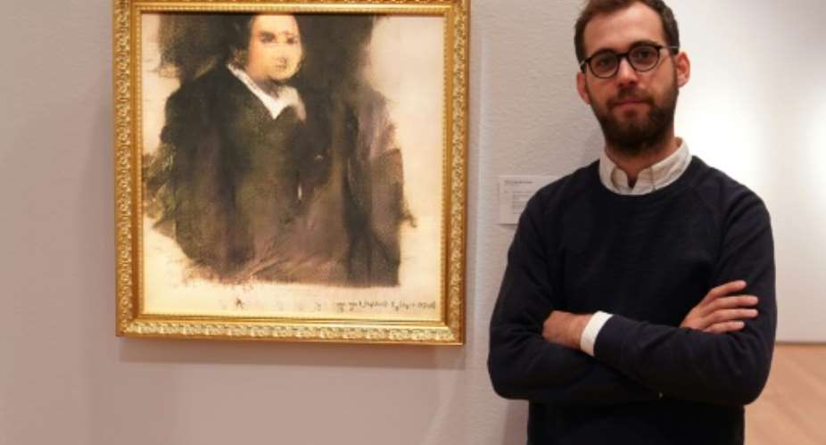 Pierre Fautrel, a member of the French art collective Obvious, poses in front of Portrait d'Edmond Belamy, an image created using Artificial Intelligence.  By TIMOTHY A. CLARY AFP