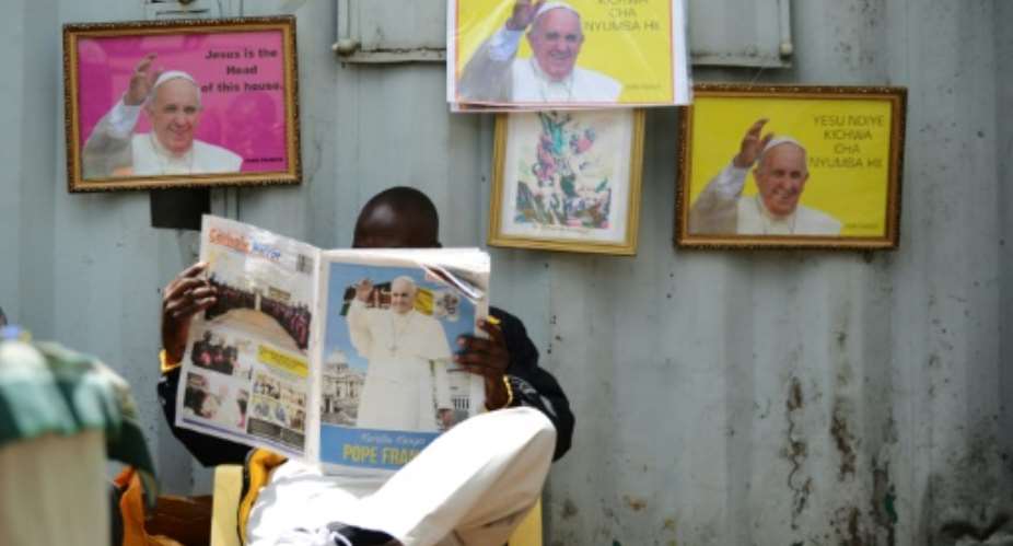 A man reads a copy of the Catholic Mirror newspaper next to pictures of Pope Francis at the Holy Family Basilica in Nairobi on November 22, 2015.  By Simon Maina AFP
